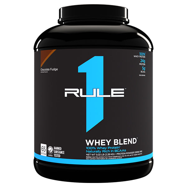 A large black container of Rule One’s Rule1 Whey Blend 5lbs displays a blue “1” and product details such as “Chocolate Fudge”, “24g protein”, “BCAAs for muscle recovery”, and “65 servings” on the front label.
